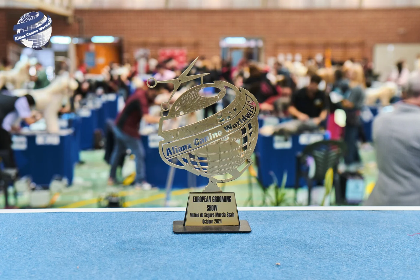 Trofeo de Alianz Canine Worldwide con una competición de peluquería canina al fondo