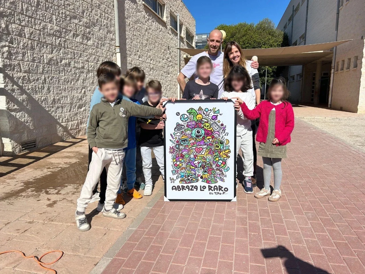 Niños y adultos sostienen una obra de El Tipo Raro con el lema Abraza lo raro